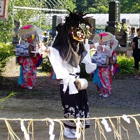 獅子頭をつけた人が手前で踊り、後ろでは笠をかぶった女性2人が太鼓をうっている写真