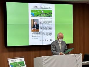 男性が米沢市オーガニックビレッジ宣言の資料をモニターにうつし、手元の資料を見ながら話している写真