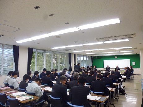 前に2人の方が着席しており、沢山の参加者が集まっている懇談会の様子を後方から写した写真