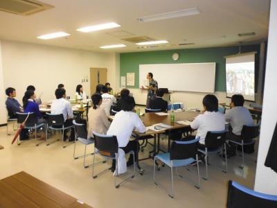 参加者が椅子に着席している部屋で、講師のかたが立って話をしている様子の写真