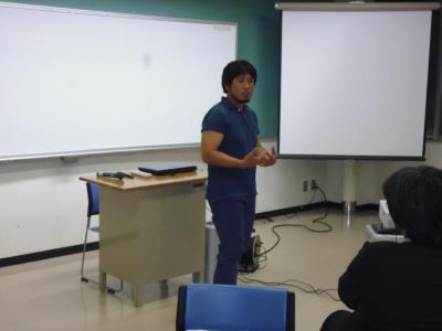 ホワイトボードやプロジェクタースクリーンが設置された部屋で、講師の方が話をしている様子の写真