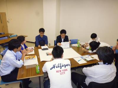 大きなテーブルの上に様々な資料を置いて、椅子に座りながら話し合いをしている様子の写真