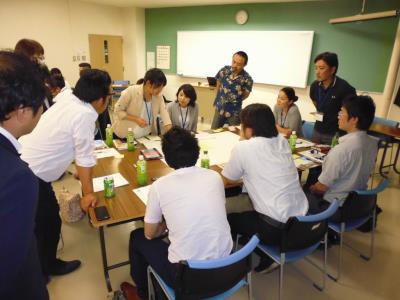 様々な資料を置いた大きなテーブルを挟んでたくさんの方たちが話し合いをしている様子の写真