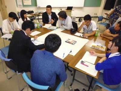 大きなテーブルの中央には大きな画用紙が置かれ、手元に置かれた用紙を見ながら話し合いを行っている様子の写真
