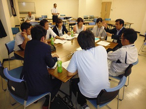 机を取り囲んで、10名くらいの班員が話し合いをしている様子を後ろから撮った写真