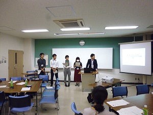 発表者5名が教壇に立ち、スクリーンに資料を映しながら発表している様子とその発表を座って聞いている人の写真