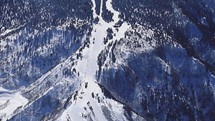 雪に覆われた山々の航空写真。尾根沿いに雪が積もり、谷間には雪解け水による白い筋が伸びている。