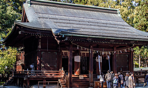 歴史を感じさせる木造建築の神社の写真。瓦屋根と重厚な木の柱が印象的で、参拝者が数人写っている。
