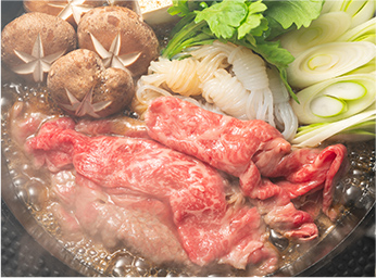 熱々のすき焼き鍋の俯瞰写真。牛肉、しいたけ、豆腐、白滝、ネギ、春菊などの具材が煮込まれ、湯気が立っている。