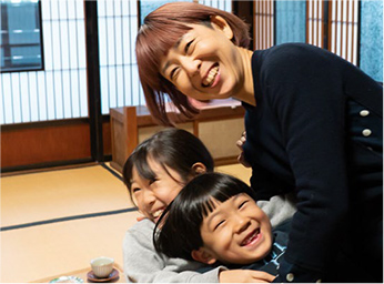 和室で、笑顔の母親が二人の子供たちを抱き寄せている写真。子供たちはそれぞれ母親の肩に顔を寄せ、三人とも楽しそうに笑っている。