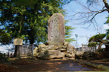 青空と木々に囲まれその中央に「従三位上杉ぎ山公之碑」と文字が彫られた大きな石碑がある写真