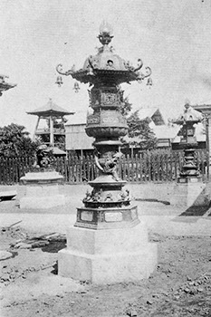 神社のような場所に、細かな装飾が施された青銅製の灯篭が建っている白黒写真