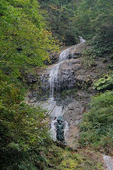 山の上の部分から水が流れている滝の下に不動尊が建っている写真