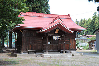 奥には民家や木々が広がっていて、その前に赤い屋根をした茶色の建物の熊野神社を正面からうつした写真