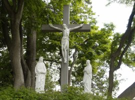 木々が生えてる中央に十字架に貼り付けにされたイエスキリストの像とその両脇に1体ずつ宣教師がキリストを見上げている像の写真