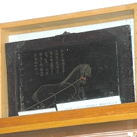 黒漆を塗った板に金蒔絵で右側を向き2本の杭に繋がれ前足をあげた神馬が描かれている絵馬の写真