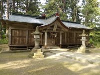 森林に囲まれ石で出来た灯篭2本の少し後ろに天満神社と書かれた立札が飾られた木造の神社がある写真