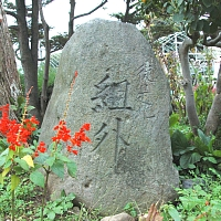 周りに草花が咲いている場所で、丸みを帯びた石碑が置かれており、石碑の中心部分には「組外」の文字が彫られている写真