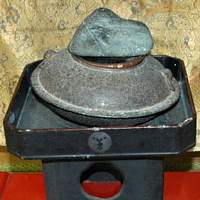 蓋のように置かれた石と鉄製の円盤型の釜「文福茶釜」の写真
