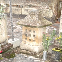 家のような形をしている正方形の部分に、9つ小さい正方形の穴があいていてる石造りの新貝弥七郎の墓の写真