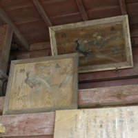 木造の天井付近の壁に雉子の絵が描かれた大きな絵馬が右上と右下に少し重なるように2枚飾られている写真