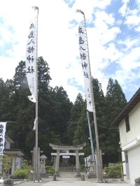 生い茂った木々を背に、中央には成島八幡神社の鳥居があり、その両端に立つ「成島八幡神社」と書かれたのぼり旗2本が写る写真