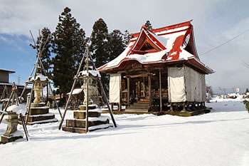威徳寺不動堂の特徴的な赤色の屋根や参道わきにある灯篭や地面などに雪が積もっている写真