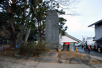 左側に大きな木が2本立っており、その横に「行在所遺趾」の文字が刻まれた大きな石碑の写真