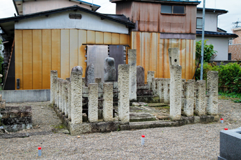 周りに民家が建ち並んでいる墓地の一角に、石柱で囲まれたお墓が設置されている写真