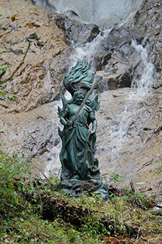 滝の水を背景に緑色の不動尊をアップで撮った写真