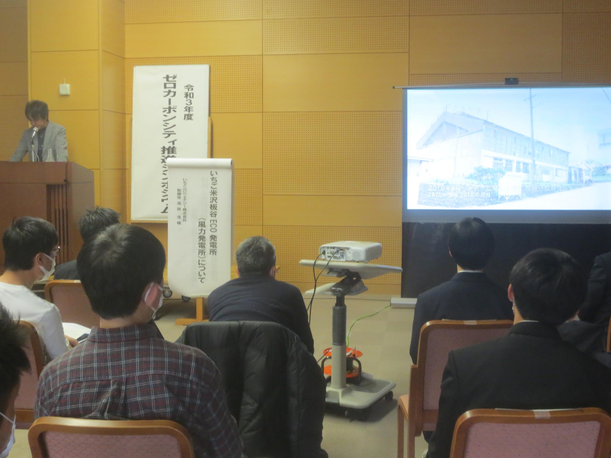 いちごECOエナジー株式会社の男性がスクリーンに映像を写し話をしているのを聞いている参加者たちの後ろ姿の写真