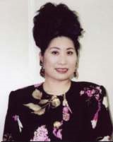 黒にピンクの花が描かれた服を着て、大きな耳飾りをし髪をを結い上げ微笑む女性あき竹城さんの写真