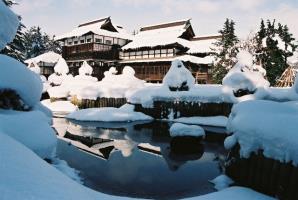 2階建ての和風造りの屋根と庭園の木に雪が積もった上杉記念館の雪景色の写真