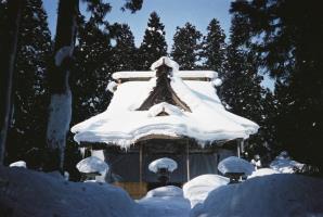 日差しが照らす青空の下、茅葺屋根が見えない程、白く厚い雪で覆われた笹野観音堂の外観写真