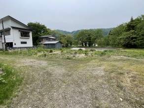 奥に住宅と木々がある広々とした空き地の写真