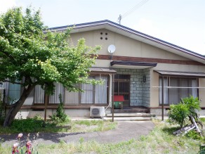 クリーム色の外壁の平屋建ての建物で、正面中央部分に玄関があり、玄関横には洗濯物を干すテラス屋根が設置されている住宅の外観写真