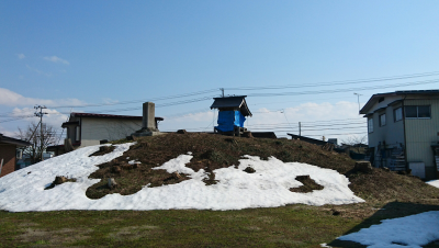 古墳の墳丘上に青いビニールシートで覆われた八幡神社が祀られており、古墳の中部から下部にかけて雪が残っている八幡塚古墳の写真