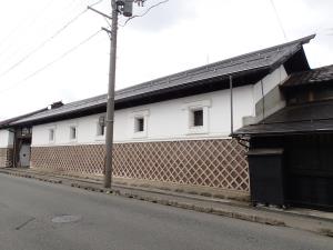 白漆喰塗の外壁の下半分が赤瓦のなまこ壁であり、長大な土蔵の小嶋総本店一号蔵を道路を挟んだ斜め向かい側から撮影した写真