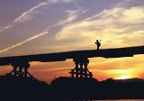 夕焼けで染まる空を背景に、橋の上を人が歩いている様子の写真