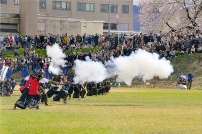 沢山の観客が見守る中、武装した人たちが一列に並び煙を出しながら発砲演武を披露する米沢藩古式砲術保存会の様子の写真
