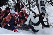 雪の積もった場所で、法被姿の男性たちが女性を投げている様子の写真