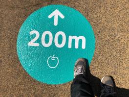 地面に緑色の丸い円の中にリンゴの絵と「200メートル」と上矢印が書かれてある印の写真