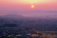 御成山公園の展望台から眺めた米沢市街地や山並みの景色が、夕焼け色にグラデーションしている写真