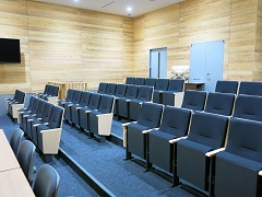 明るい色合いの木材を使用した壁とトーンダウンした青色の椅子が4つ横に並び、4段に分かれて設置されている傍聴席の写真