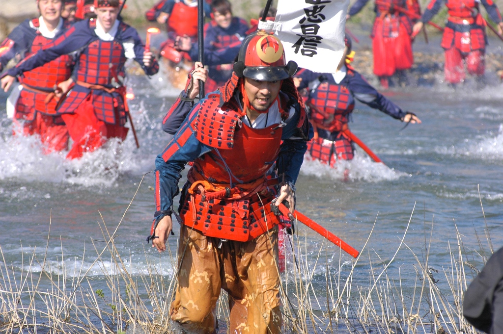 赤い甲冑を着た武者たちが川を走って渡っている写真