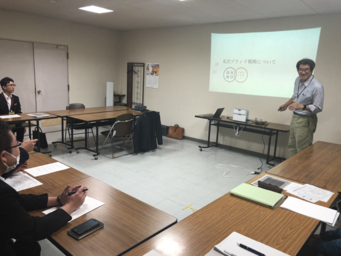 スクリーンを使って講演する伊藤室長とその話を聞いている参加者たちの写真