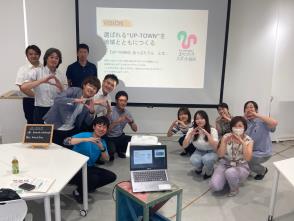 まちづくりスポット仙台で参加者がスクリーンをバックに両サイドに分かれて、胸の前で三角ポーズをしている集合写真