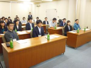椅子に着席して講話を聴講する参加者たちを正面左側から撮った写真