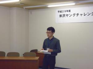 黒いシャツ姿の男性が紙を両手に持ちながら前に立ち、参加者に向けて自己紹介をしている様子の写真