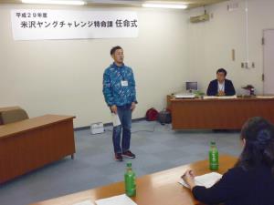 青いブルゾンを着た男性が正面に立ち、紙を片手に正面を向いて参加者に向けて自己紹介をしている様子の写真